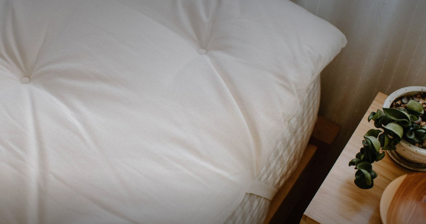 A tufted organic cotton mattress topper on a bed beside a wooden nightstand